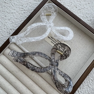 Detail of bow-shaped hair claws with lace patterns and gold springs on a soft beige tray