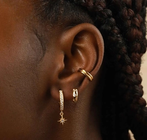 Detail of star pendant earrings and gold pave ear cuffs worn together for a layered look