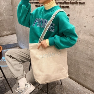 Detail of canvas tote bag with smile embroidery and colorful woven shoulder strap