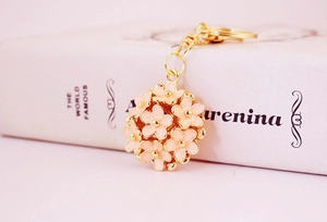 Close-up of pink enamel flower cluster keychain with gold plating on a white book