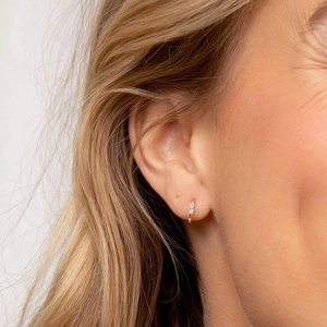 Close-up of golden curved wave hoop earrings with rectangular clear zircon inlays
