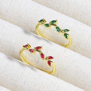 Close-up of gold leaf vine rings with emerald and ruby zircon stones on beige fabric