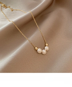 Close-up of three elegant white pearls and gold beads on a delicate chain necklace
