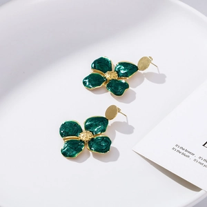 Green enamel leaf drop earrings with gold plating on a minimalist white ceramic tray