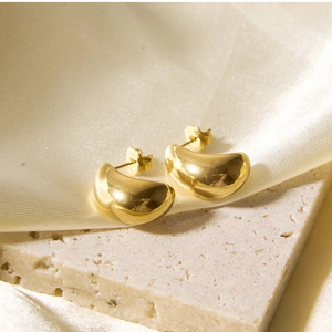 Close-up of golden bean-shaped earrings on beige stone and silk background
