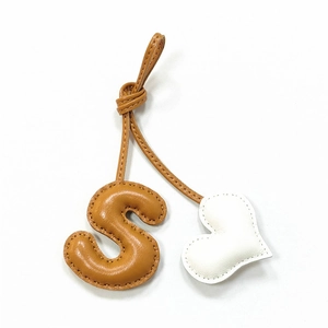 Detail of handmade leather bag charm with stitched letter S and white heart pendant