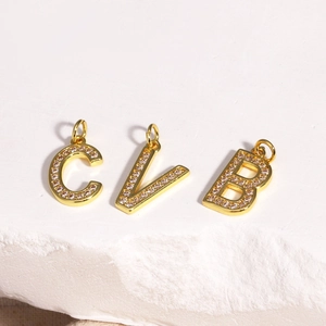 Close-up of golden letter pendants C, V, B with inlaid cubic zirconia on stone
