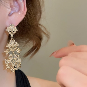 Detail shot of hollowed-out gold flower drop earrings with a three-layer textured finish