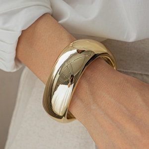 Macro shot of wide chunky gold-finished geometric bangle on a woman wrist