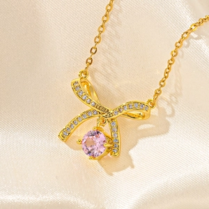 Close-up of golden bow necklace featuring a pink gemstone and shimmering micro-pavé zircons