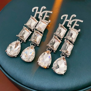Detail view of silver drop earrings with HE initials and square crystals on green leather