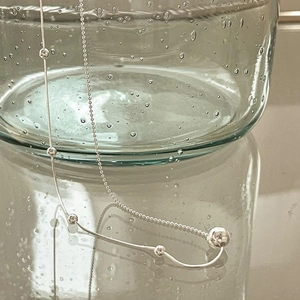 Close-up of minimalist 925 sterling silver ball necklace near a glass with bubbles