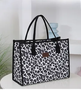 Detail of large leopard print tote bag with black canvas handles on a white table