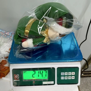 Detail shot of a green Christmas elf plush showing a weight of 214.7g on a scale