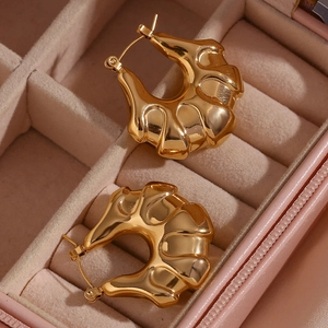 Detailed macro shot of 18K gold-plated textured hoop earrings on a soft pink velvet tray