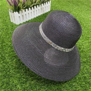 Detail of black straw sun hat with rhinestone band and metal M logo on green grass