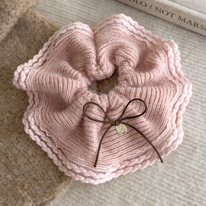 Detail of pink knitted lace scrunchie with a brown bow and gold logo charm on it