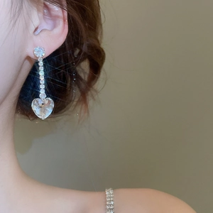 Close-up of silver tassel earrings with heart-shaped crystal pendant on model