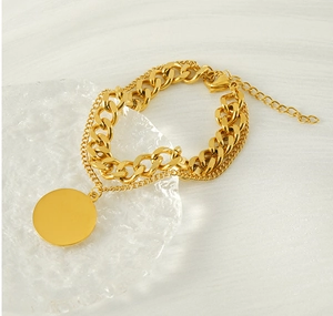 Detail of gold titanium double-layered chain bracelet with smooth round pendant on glass
