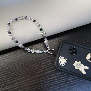 Detailed macro view of beaded phone strap with pearls and floral charms on a black case