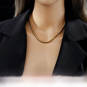 Close-up of a minimalist golden snake chain necklace on a model wearing a black blazer