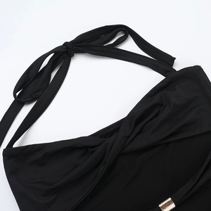 Detail of black halter dress featuring metallic gold buckle and pleated cross chest design
