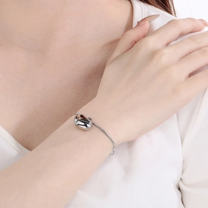 Close-up of a silver-toned sleek bean pendant on a delicate snake chain bracelet