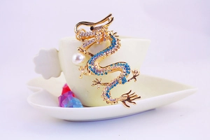 Detailed view of a golden dragon keychain with blue rhinestones and a white pearl accent
