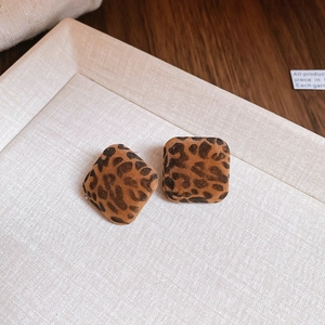 Macro shot of square leopard print earrings in brown flocking on a beige textured tray