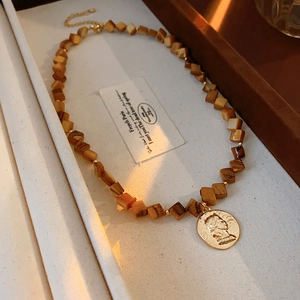 Macro detail of vintage gold portrait relief charm with earthy brown cubic beads necklace