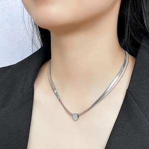 Detail of a layered silver snake chain necklace with a minimalist geometric rectangular pendant