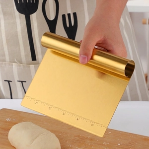 Golden stainless steel dough scraper with measurements being used on a wooden board