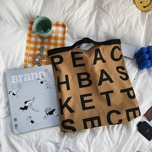 Close-up of khaki canvas tote bag with bold letter print on a stylish lifestyle background