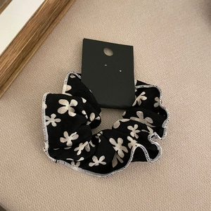 Black floral scrunchie with white flower print and fabric texture on beige background