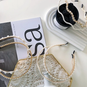 Detailed view of three golden metal wavy pearl headbands on an aesthetic tray