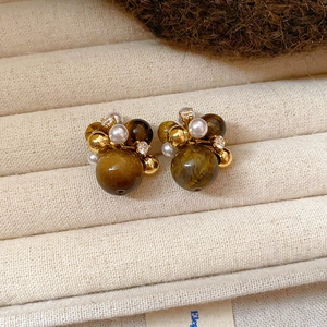 Detailed view of vintage tiger eye stud earrings with pearls and gold beads on fabric