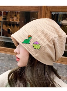 Close-up of cute cartoon dinosaur pins decorated on a beige knitted beanie hat