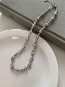 Detailed shot of silver bead necklace with zircon star charms on a white ceramic plate