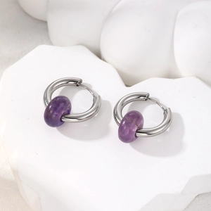 Detail of silver hoop earrings with natural purple amethyst beads on a white stone base