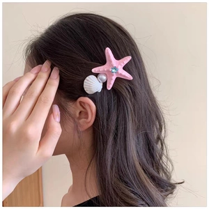Detail of pink starfish hair clip with white shell and pearl on dark brown hair