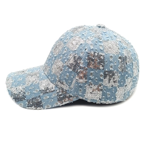 Detail of light blue denim baseball cap featuring silver sequin checkered patterns and frayed edges