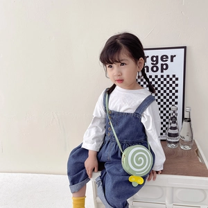 Kids green lollipop crossbody bag with yellow bow modeled on denim overalls