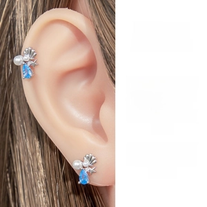 Detailed view of ocean theme cartilage stud with blue zircon and shell on human ear