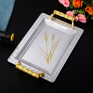 Detail of silver rectangular tray with golden handles and wheat ear pattern on black surface