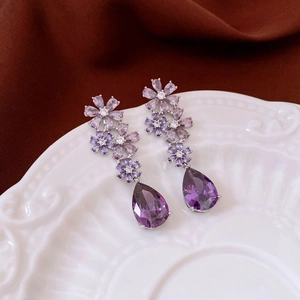 Macro detail of purple crystal flower earrings with pear-cut drop stones on white ceramic