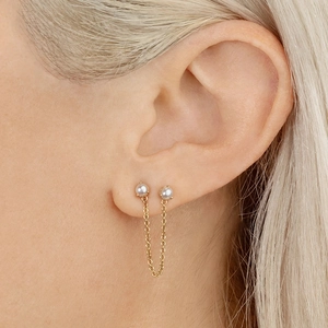 Elegant gold double piercing earrings with pearls and a delicate dangling chain