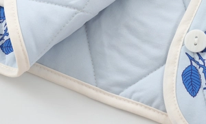Detail of light blue quilted fabric with leaf pattern, white buttons and stitched edges