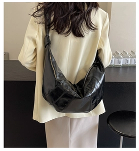 Detail of black glossy croissant bag with quilted design and knotted shoulder strap