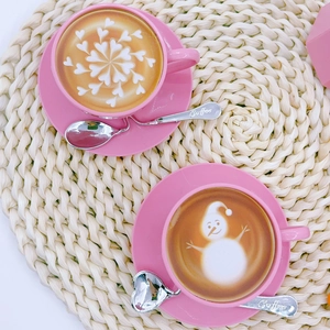 Top view of pink ceramic coffee cups with snowflake latte art and silver heart spoons