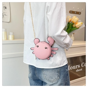Pink crab shaped mini crossbody bag with gold chain strap shown in a cafe setting